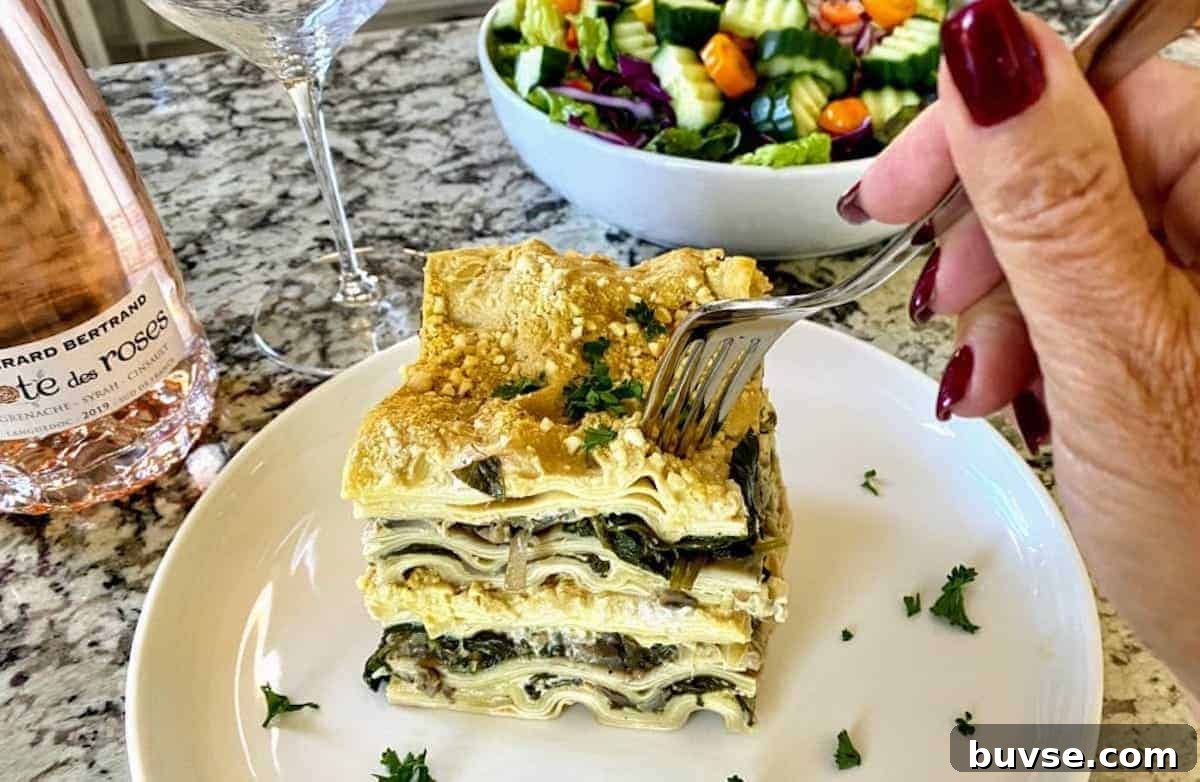 Creamy Vegan White Sauce Lasagna Recipe 11 White sauce lasagna on a plate on the table with a salad, a wine glass, and a bottle of rose wine.