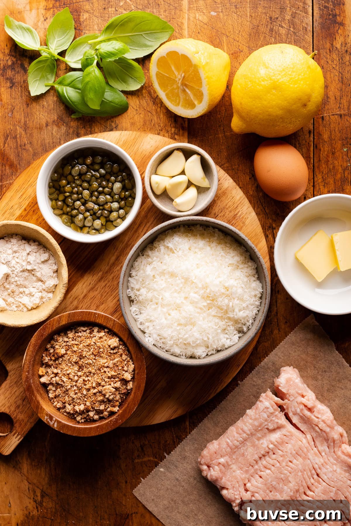 Ingredients for chicken piccata meatballs arranged on a wooden board in different sized bowls. 