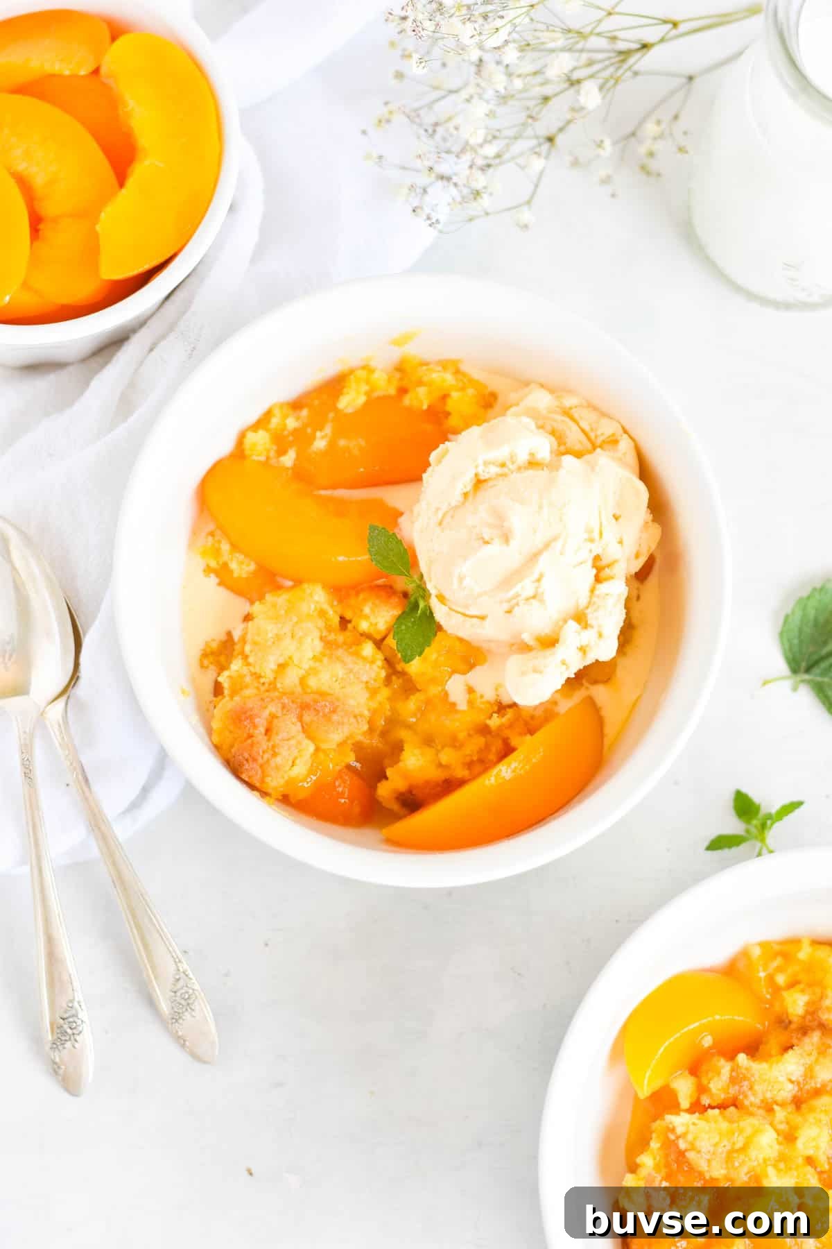 Quick Peach Cobbler with Canned Peaches and Cake Mix 2 peach cobbler in white bowl with vanilla ice cream on top.