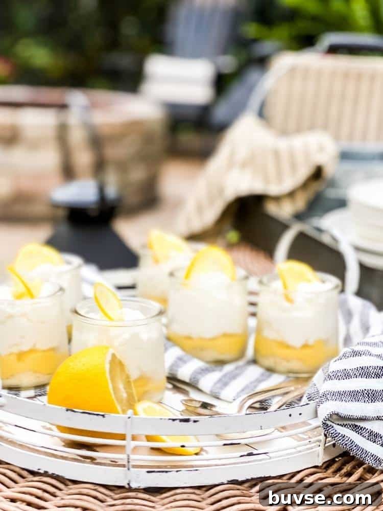 Refreshing Summer Picnic Menu Ideas to Wow Guests 2 Six small clear glass jars of Lemon Bar in a Jar sitting on a white wood and metal serving tray with spoons and a striped tea towel on a wicker table at an outdoor picnic.