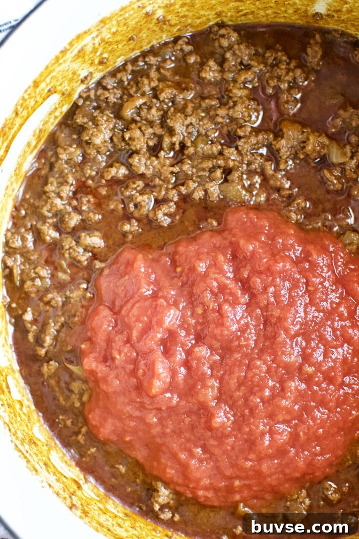 Adding crushed tomatoes to the pot to finish the chili.