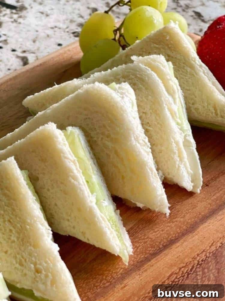 Refreshing Summer Picnic Menu Ideas to Wow Guests 5 Wood cutting board with 5 cucumber sandwiches on white bread cut in triangles with the crusts removed. Fresh grapes and strawberries garnish the board