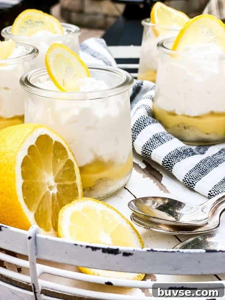 Refreshing Summer Picnic Menu Ideas to Wow Guests 8 Five small clear glass jars of Lemon Bar in a Jar sitting on a white wood and metal serving tray with spoons and a striped tea towel. A cut lemon is the garnish.