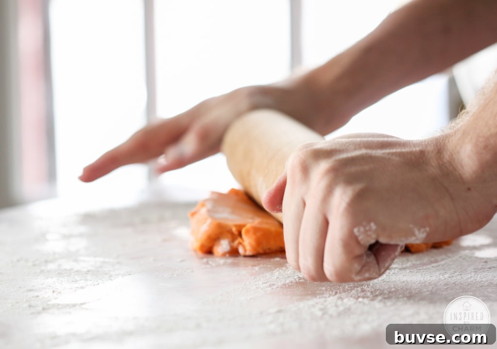 hands with a rolling pin rolling out orange cookie dough.