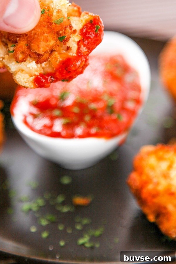 a deep fried macaroni and cheese ball being dipped into a bowl of marinara sauce.