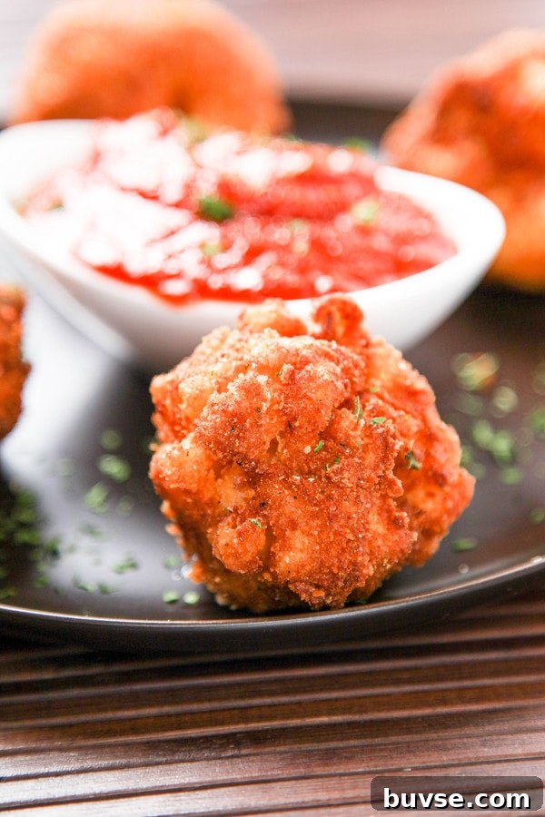 a black plate with a mac and cheese fritter with a bowl of marinara sauce in the background.