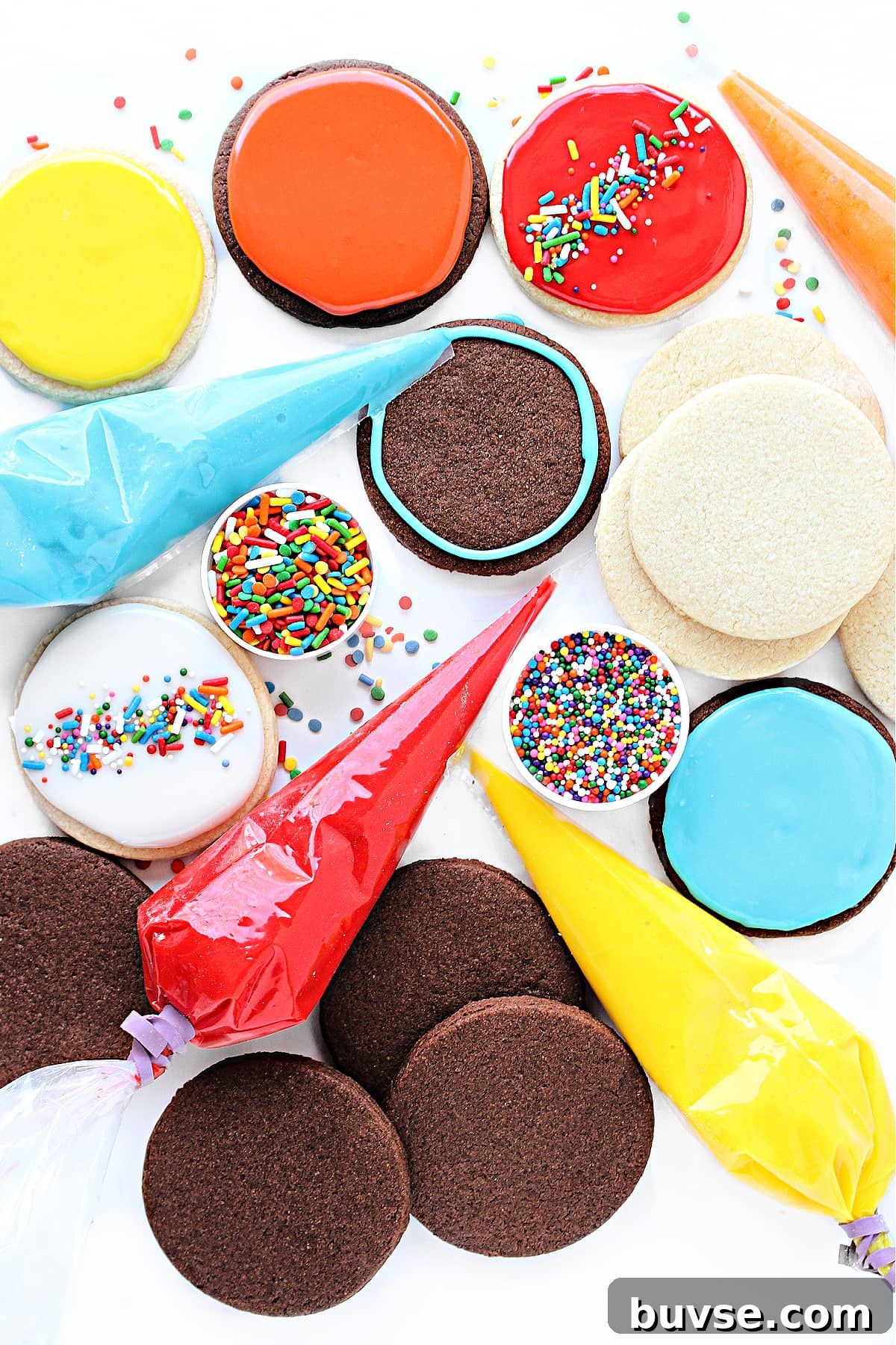 Glaze Icing Recipe for Cakes, Donuts, and Pastries 2 Colorful icing glaze in piping bags, chocolate and vanilla sugar cookie circles, and sprinkles.