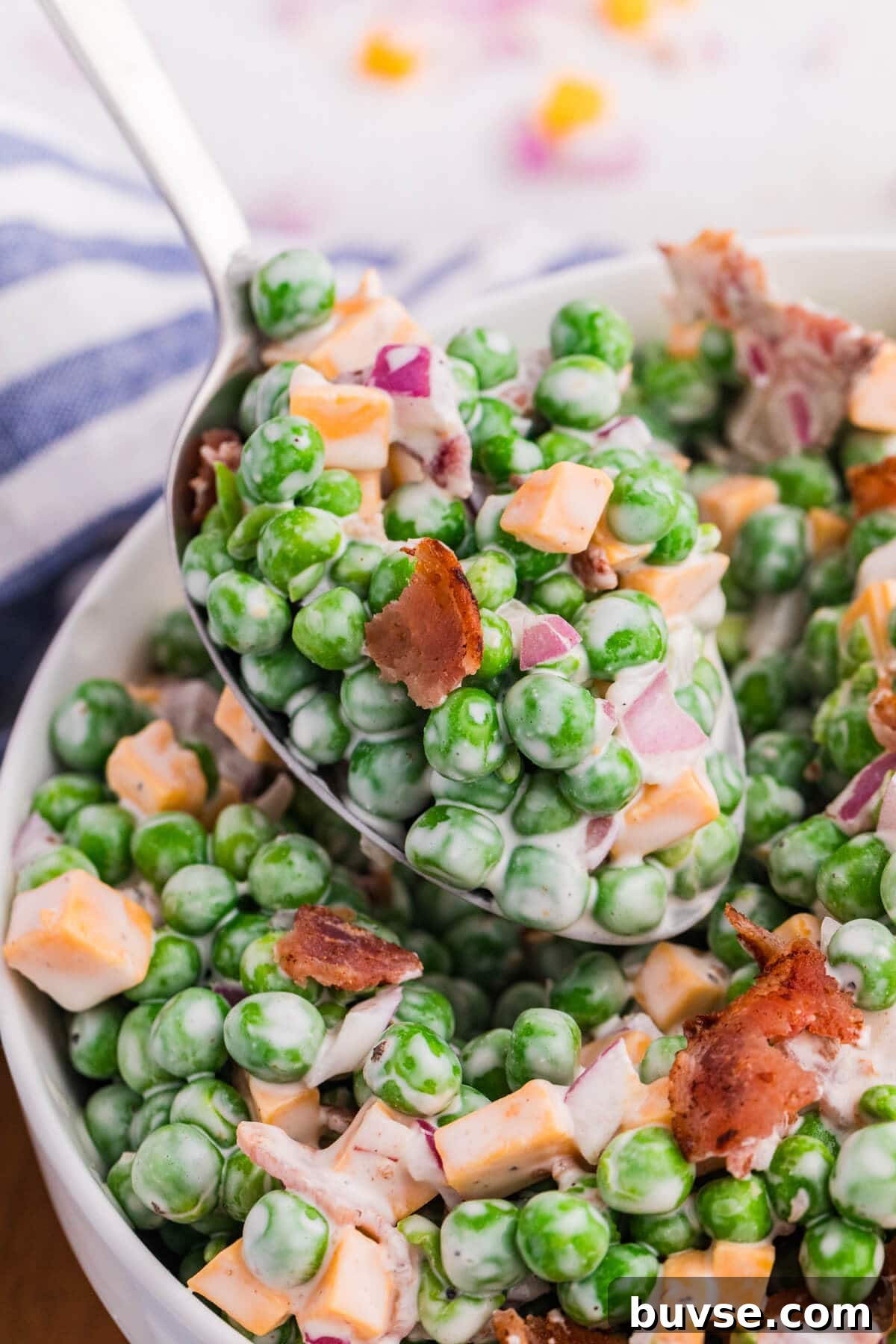 Macro close-up of spoonful of creamy pea salad with green peas, cheddar cheese, crispy bacon, and red onion coated in dressing, detailed texture food photography.