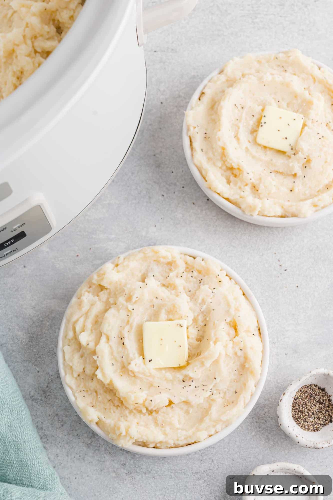 Mashed potatoes in two bowls by a crockpot.