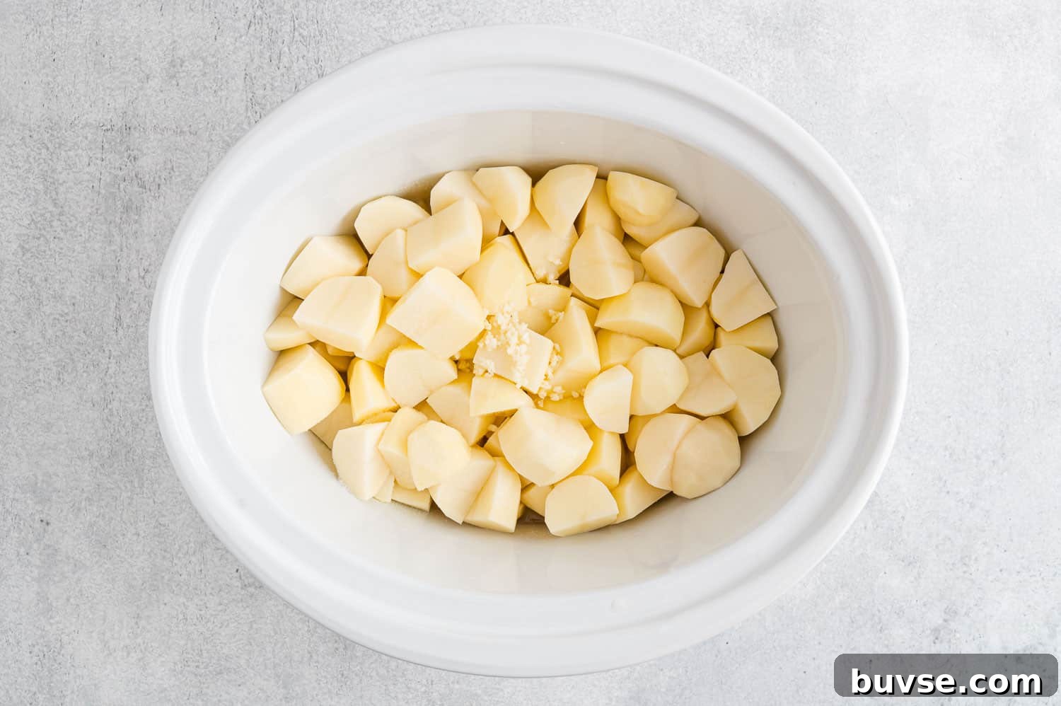 Uncooked peeled potatoes in a crockpot.