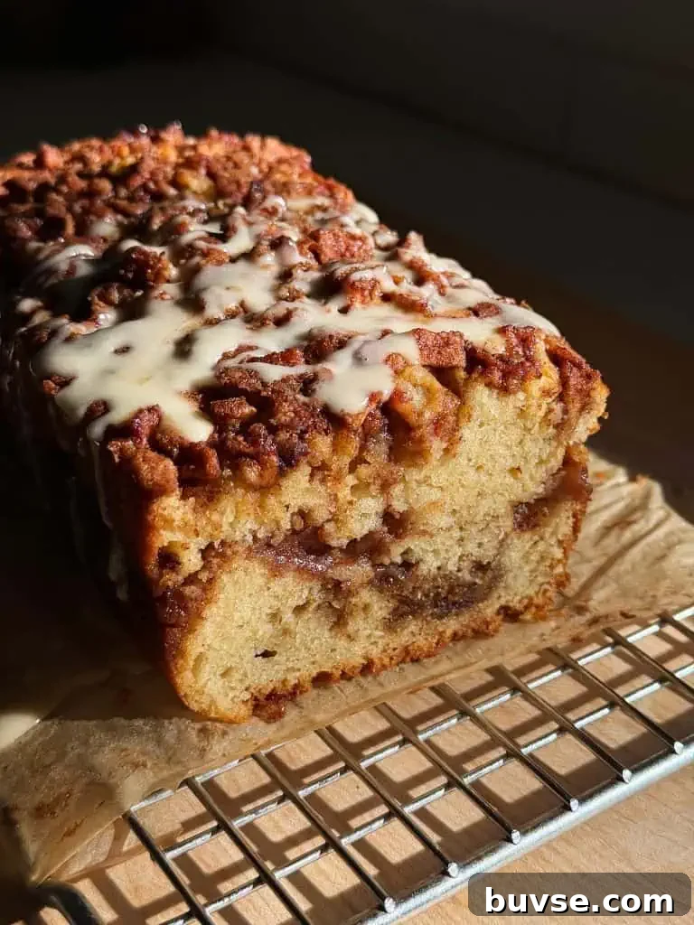 A glazed apple fritter loaf cake on parchment with a slice cut to reveal the moist apple-filled center.
