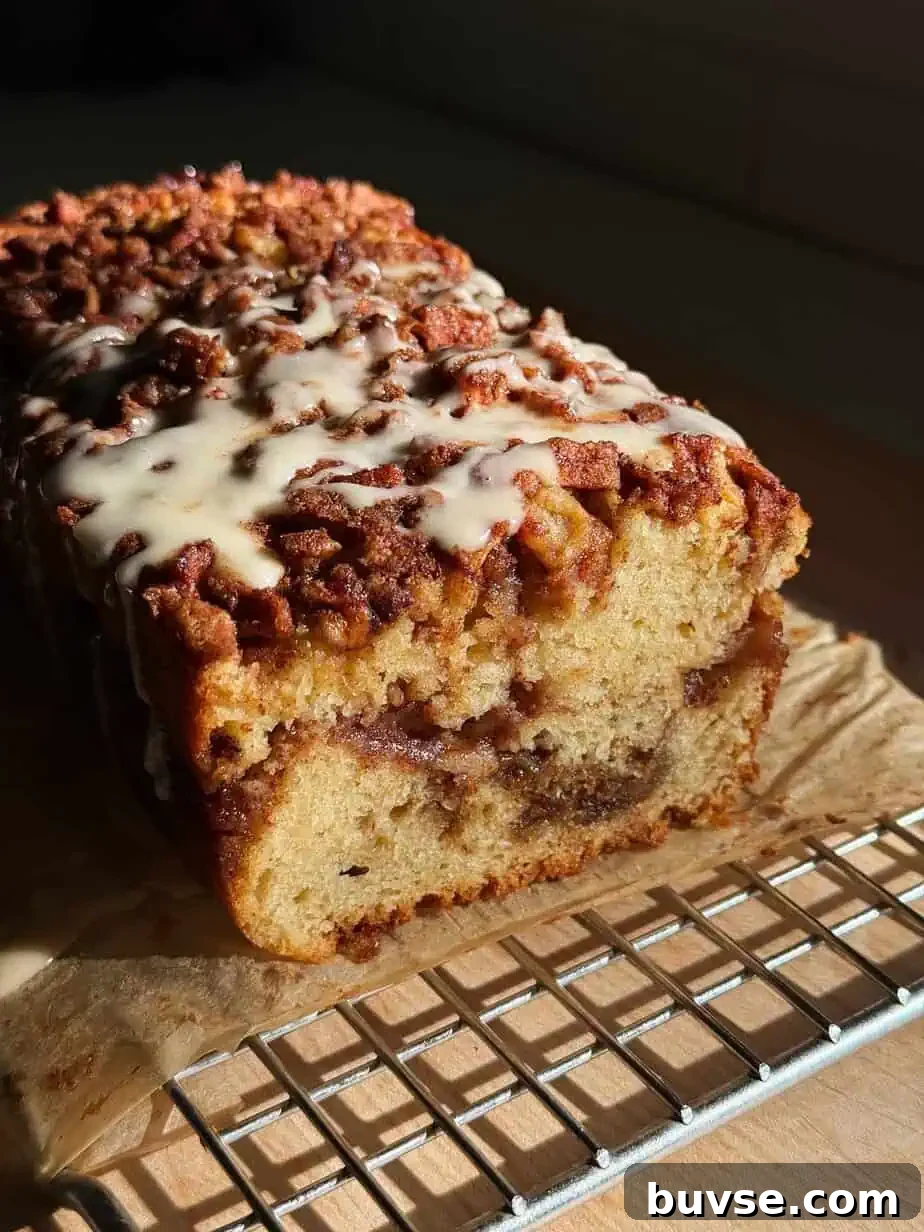 A glazed apple fritter loaf cake on parchment with a slice cut to reveal the moist apple-filled center.
