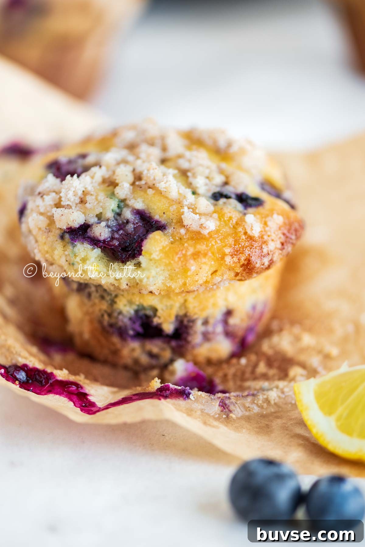 Bakery-Style Lemon Blueberry Muffins with Streusel Topping 12 Unwrapped lemon blueberry streusel muffin with lemon wedges and blueberries around it | All images © Beyond the Butter®