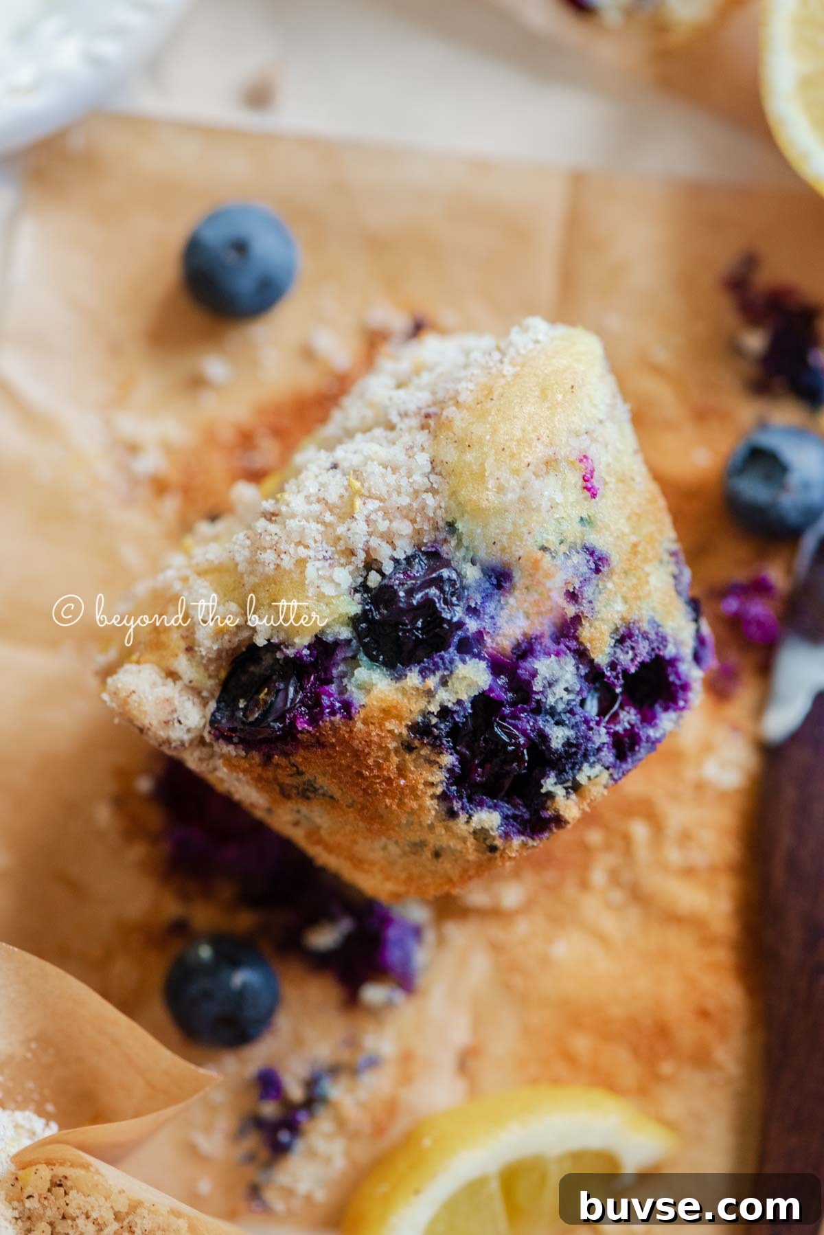 Bakery-Style Lemon Blueberry Muffins with Streusel Topping 3 Unwrapped lemon blueberry streusel muffin with lemon wedges and blueberries around it | All images © Beyond the Butter®
