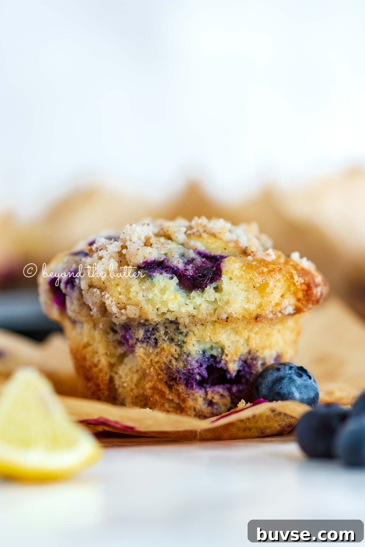 Bakery-Style Lemon Blueberry Muffins with Streusel Topping 6 Unwrapped lemon blueberry streusel muffin with lemon wedges and blueberries around it | All images © Beyond the Butter®