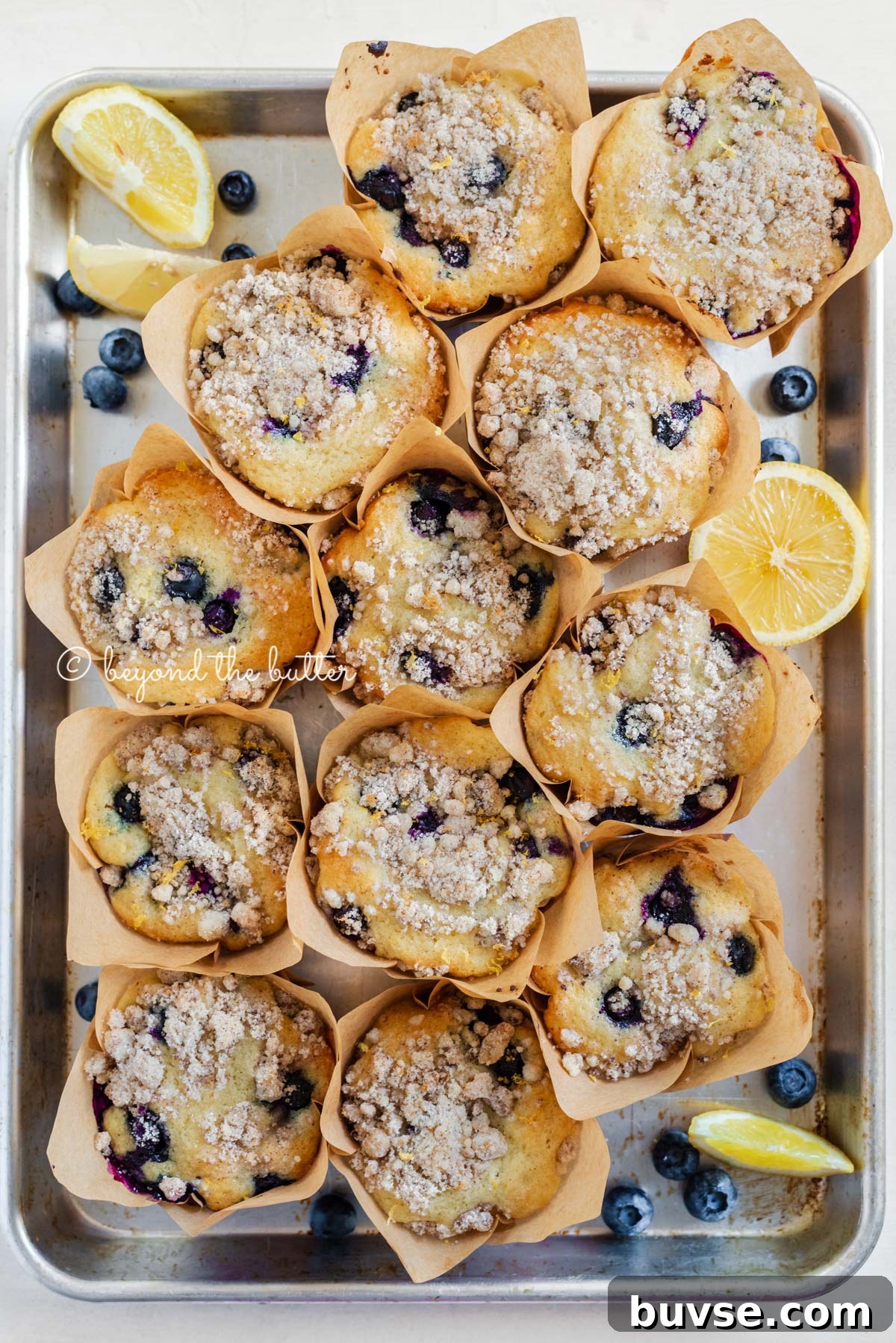 Bakery-Style Lemon Blueberry Muffins with Streusel Topping 10 Baking tray filled with bakery style lemon blueberry muffins garnished with slices of lemons and blueberries | All images © Beyond the Butter®