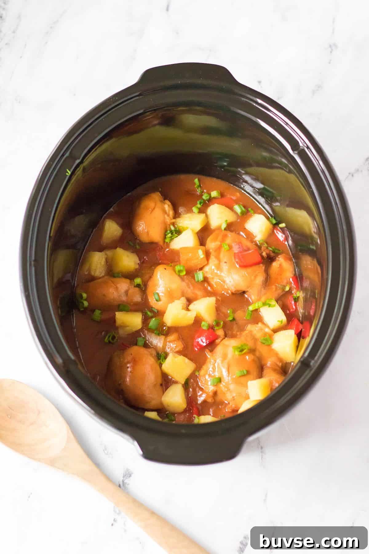Cooked Hawaiian chicken in the crockpot topped by sliced green onion.