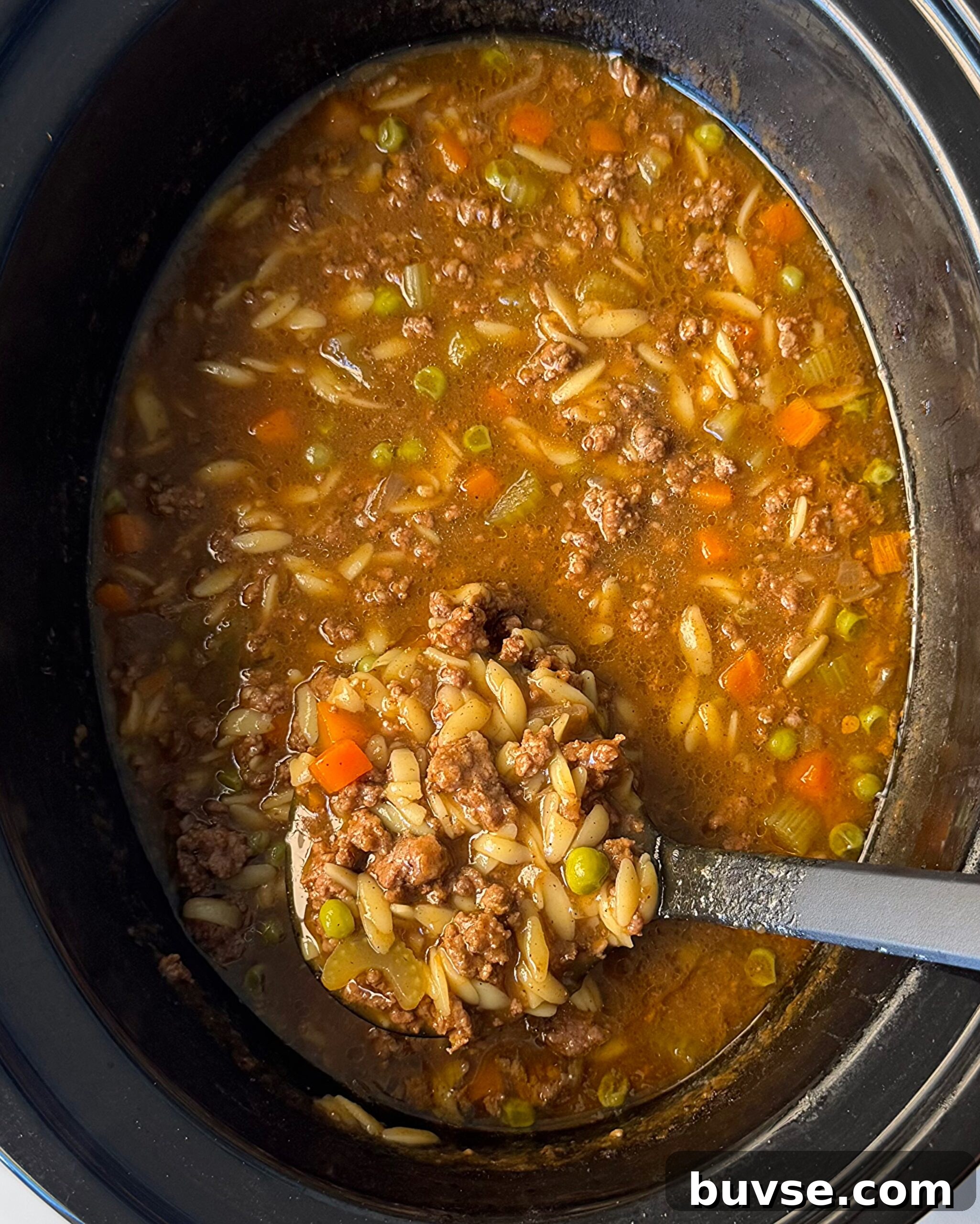 Slow Cooker Beef and Pumpkin Orzo Soup 2 overhead shot of cooked Beef Pumpkin Orzo Soup in a black slow cooker with a black spoon