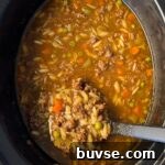 overhead shot of cooked Beef Pumpkin Orzo Soup in a black slow cooker with a black spoon