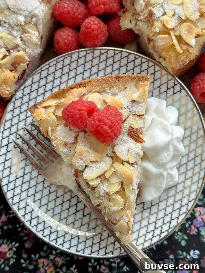 a slice of raspberry almond cake with a side of whipped cream, plated and ready to serve