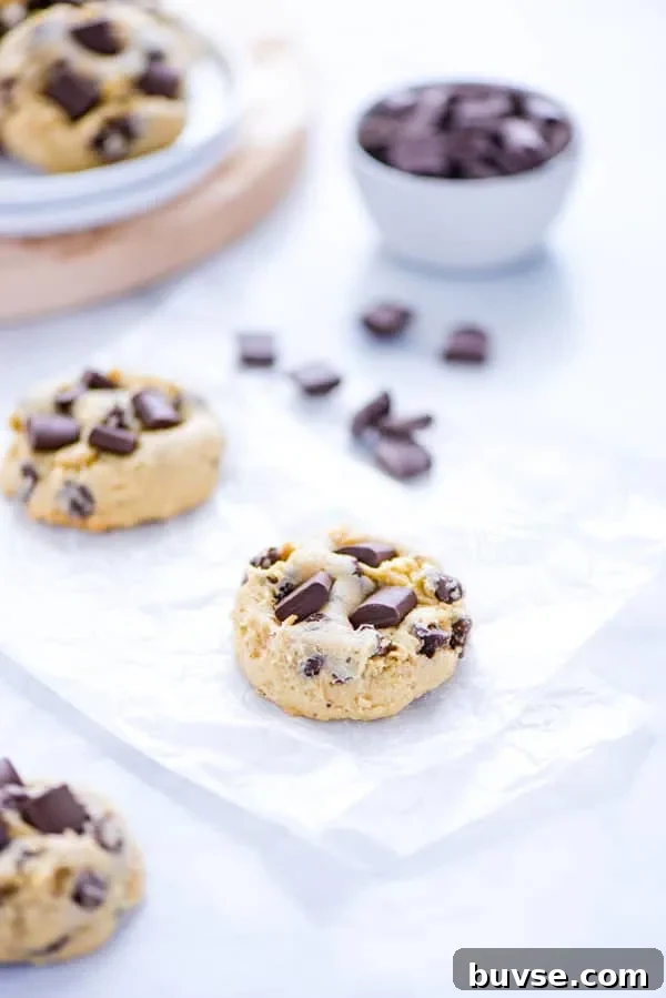 Gluten-Free Sourdough Chocolate Chip Cookies Recipe 4 Gluten Free Sourdough Chocolate Chip Cookies on white parchment paper with chocolate chunks and a plate of cookies in the background
