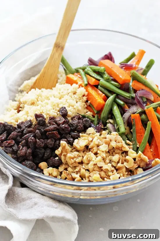 A large glass bowl filled with couscous, roasted veggies, walnuts and raisins.