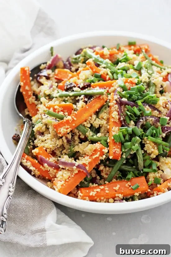 A white bowl filled with Vegan Couscous Salad and a silver spoon on the side.
