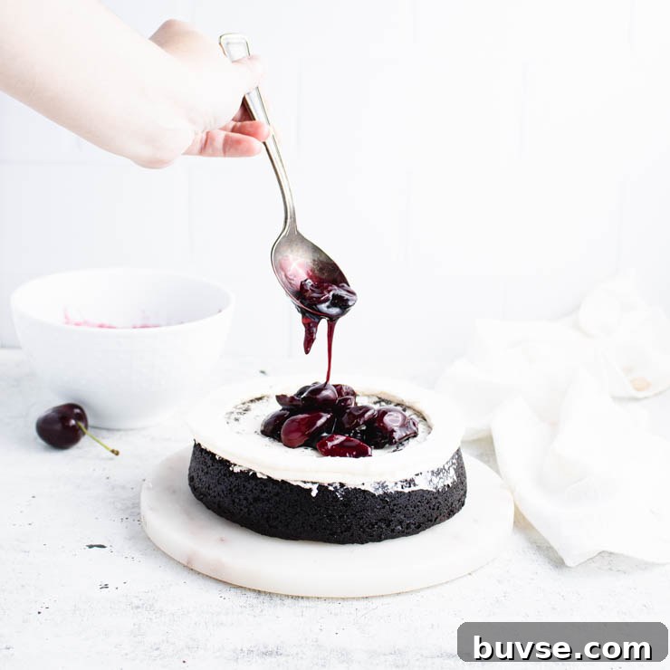 cherry compote being spooned into the center of a frosted layer of cake.