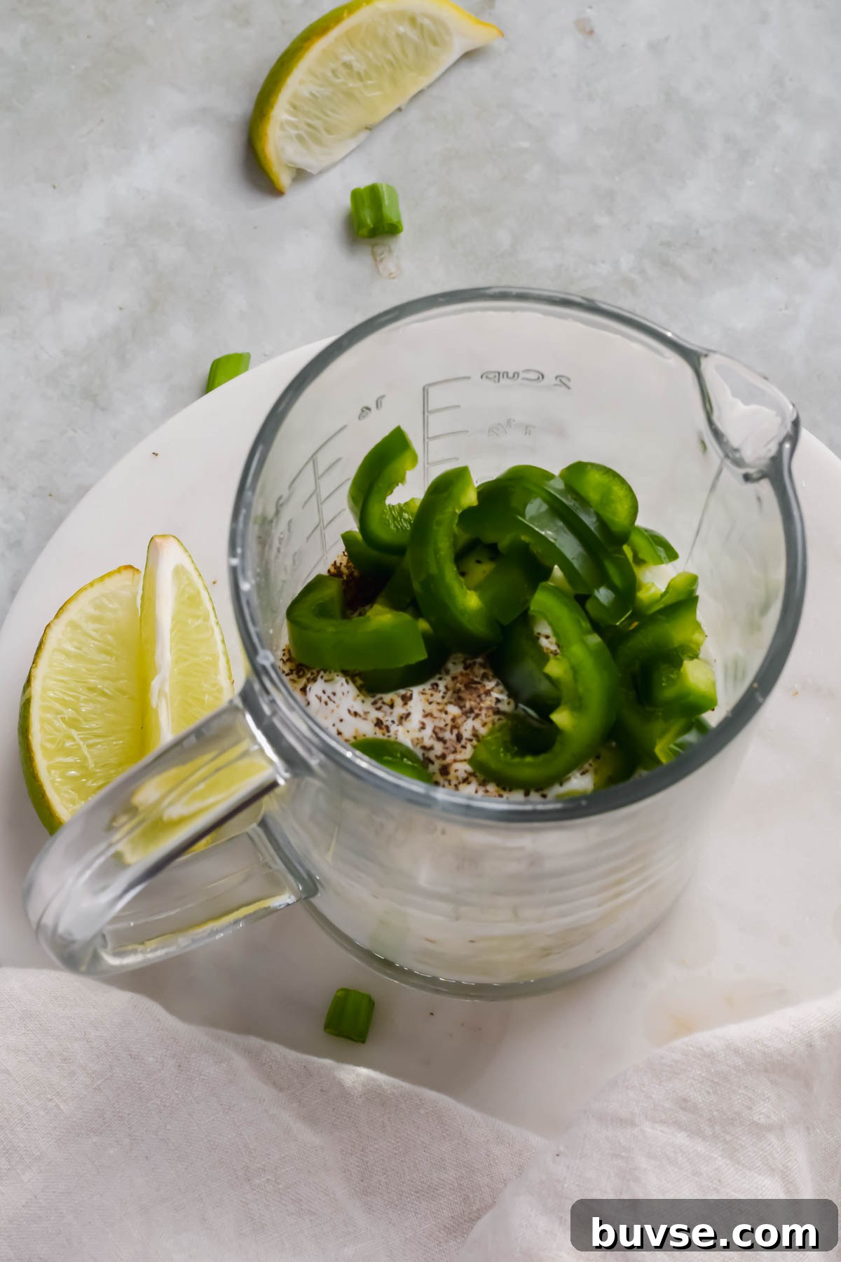 Homemade Creamy Jalapeno Sauce for Tacos and Dips 5 jalapenos and herbs added to yogurt dressing mixture in glass measuring cup.