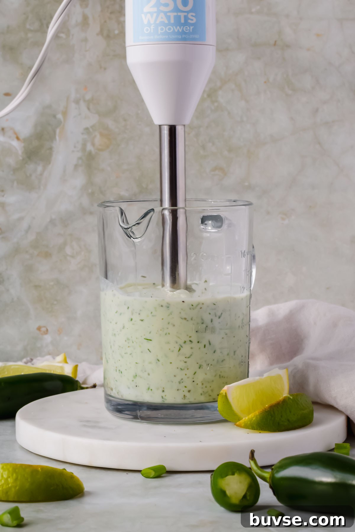 Homemade Creamy Jalapeno Sauce for Tacos and Dips 6 immersion blender in glass measuring cup blending creamy jalapeno sauce.