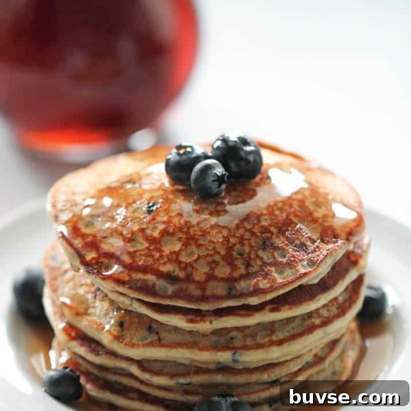 A stack of Blueberry Protein Pancakes on a plate topped with butter and fresh blueberries.