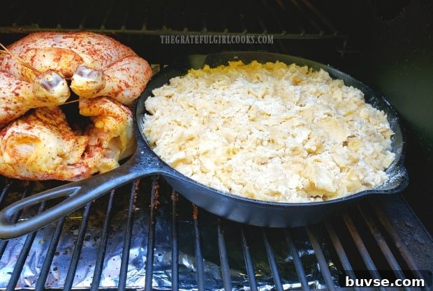 A cast iron skillet full of cobbler is placed onto a Traeger grill, next to roasting chicken.