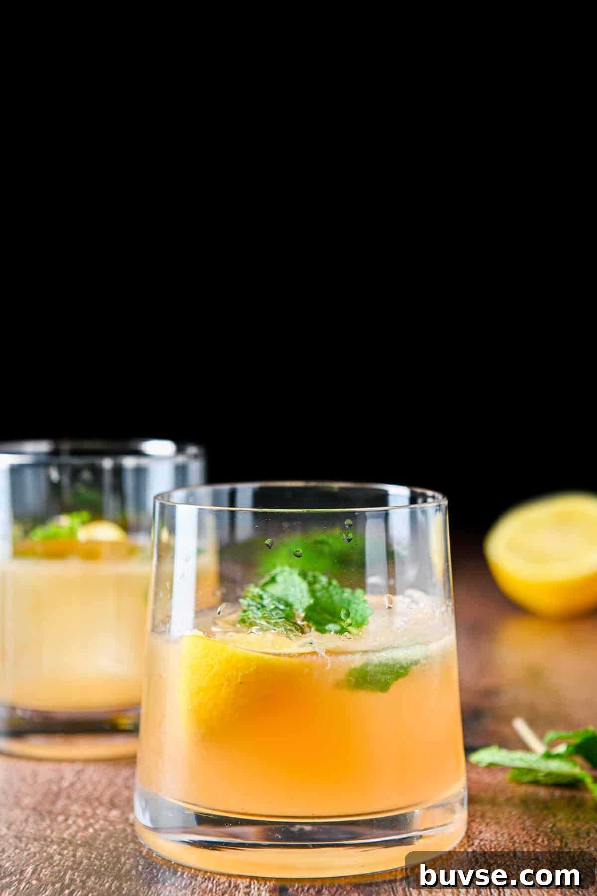 A sloped glass with the whiskey drink with lemon and mint in front of another