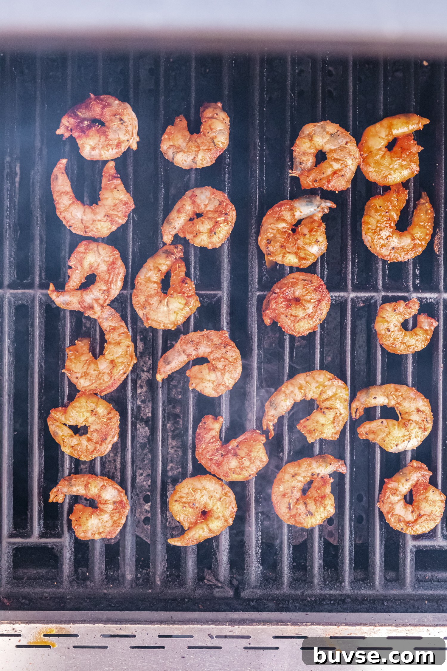 Spiced shrimp cooking on a grill, arranged in rows with visible grill marks.