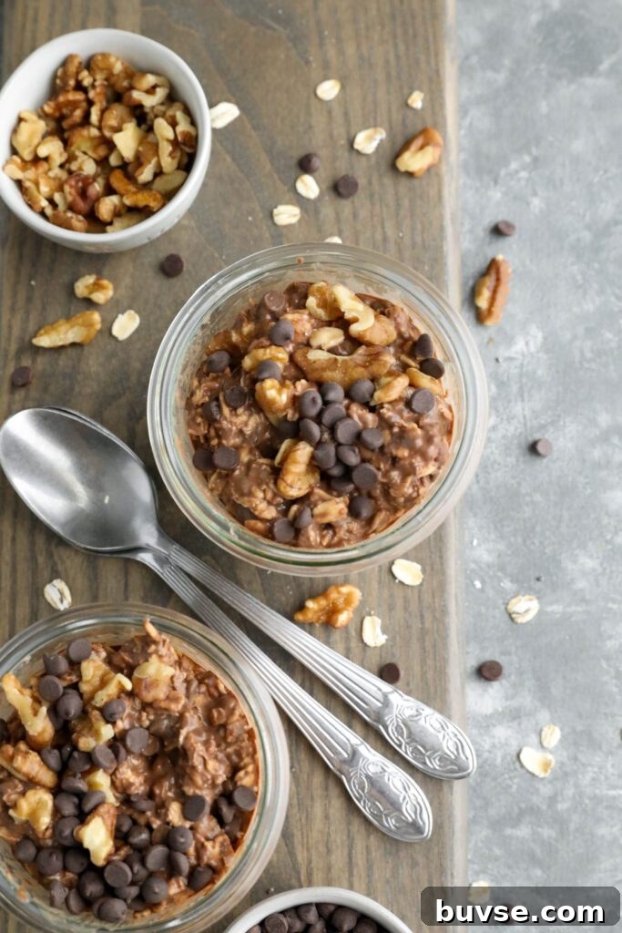 Brownie Batter Overnight Oats Recipe for Chocolate Lovers 11 Brownie Batter Overnight Oats served in mason jars on wooden board surrounded by chocolate chips and chopped walnuts with two spoons