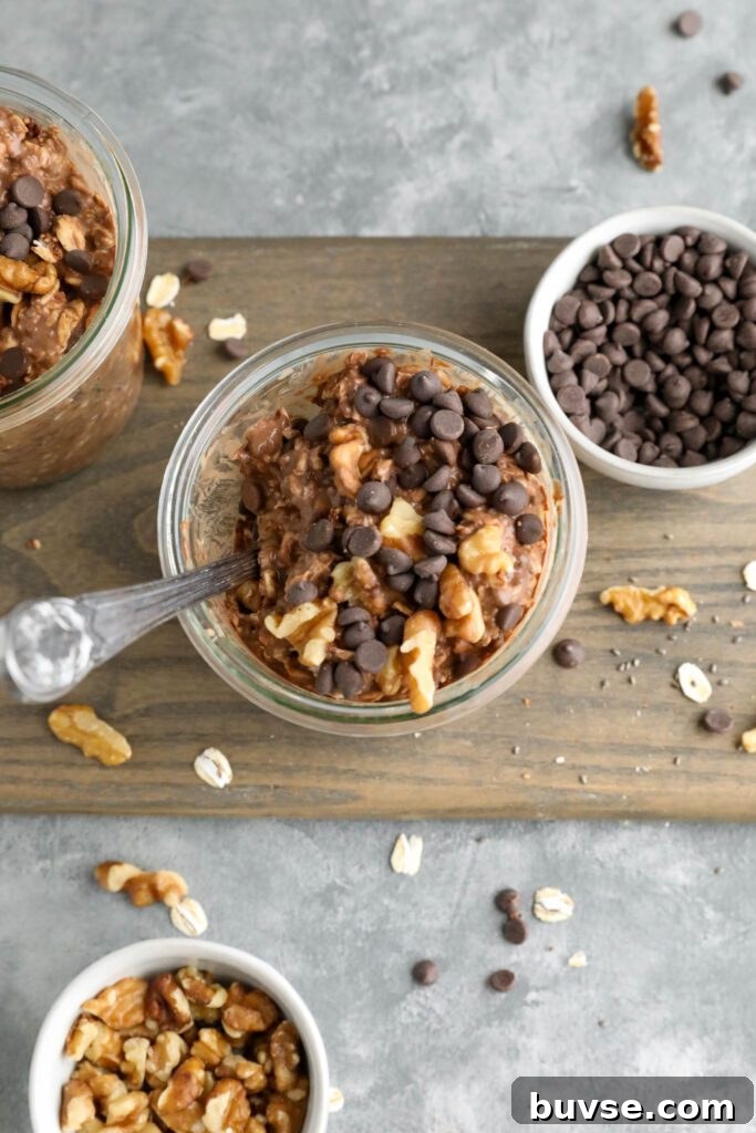 Brownie Batter Overnight Oats Recipe for Chocolate Lovers 12 Brownie Batter Overnight Oats served in mason jars on wooden board surrounded by chocolate chips and chopped walnuts with two spoons