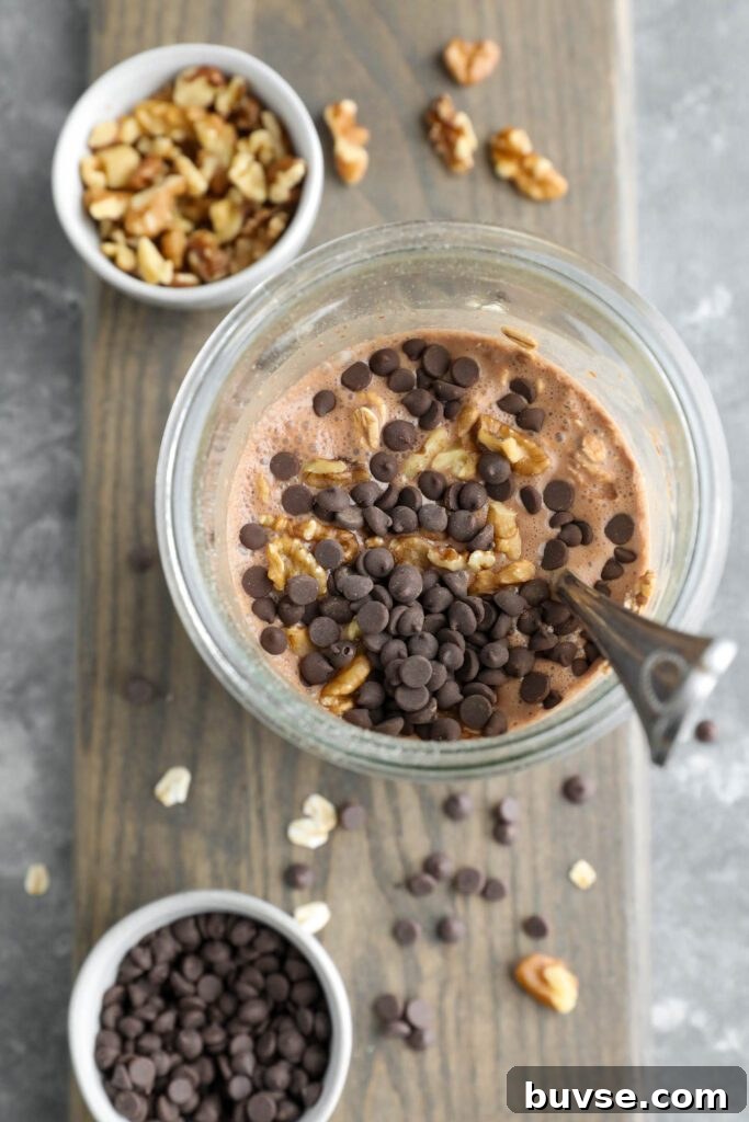 Brownie Batter Overnight Oats Recipe for Chocolate Lovers 8 brownie batter overnight oats mixed in mason jar on wooden board with dark chocolate chips and walnuts mixed in with spoon