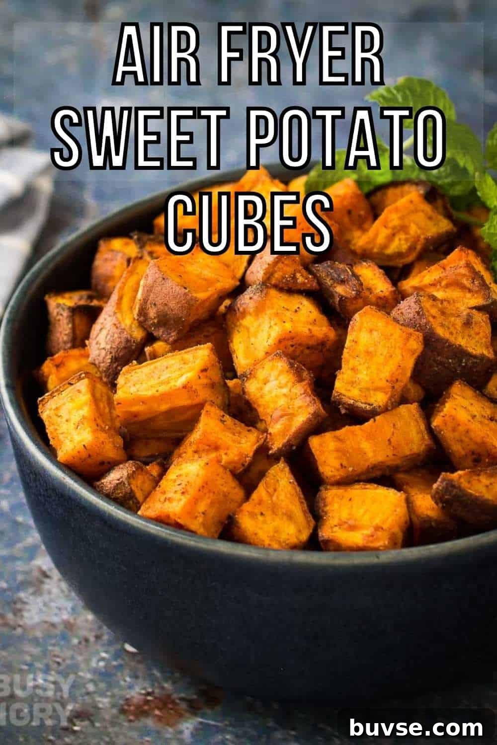 Side shot of sweet potato cubes in a black bowl garnished with basil on a blue and grey marble surface.