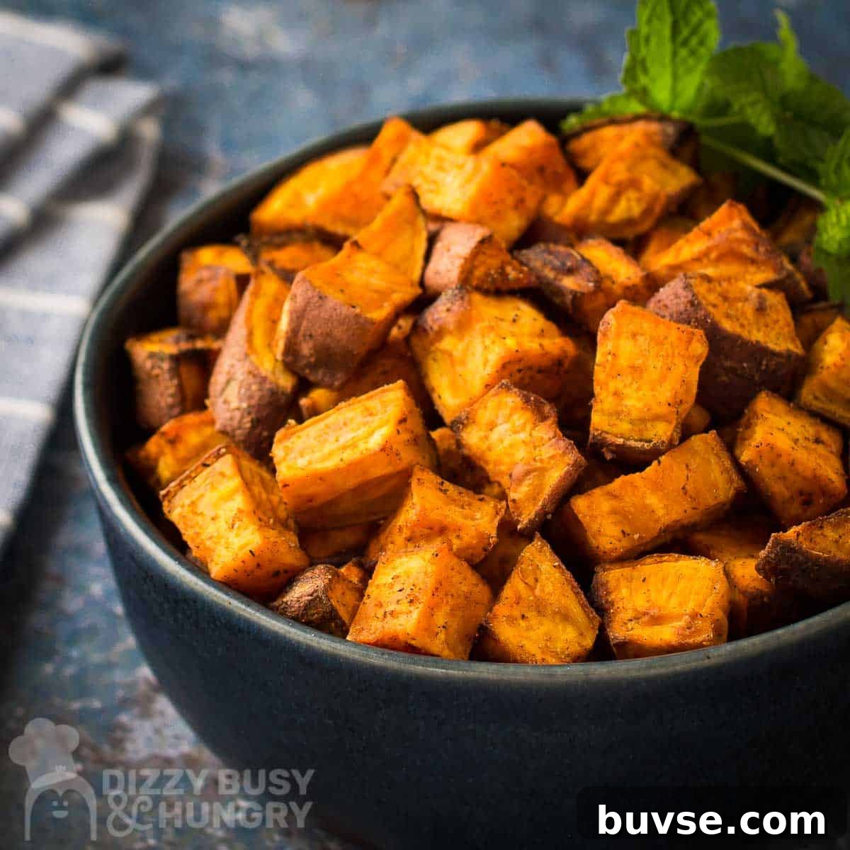 Side shot of sweet potato cubes in a black bowl garnished with basil on a blue and grey marble surface.