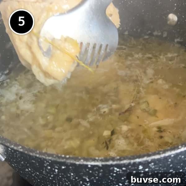 Greek Lemon Orzo Soup with Chicken | cookeatworld.com a pan of soup bubbling. tongs hold a chicken thigh as it is removed from the pan.