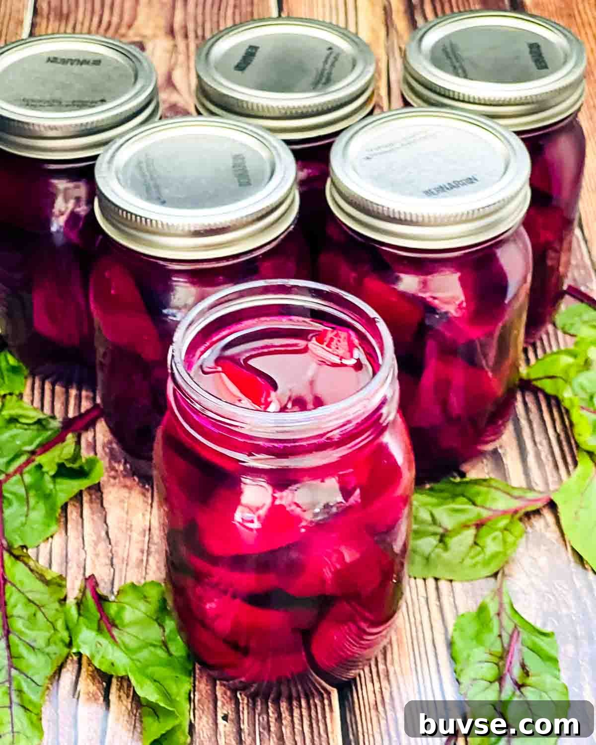 Homemade Old-Fashioned Pickled Beets Recipe 17 Six jars of canned beet pickles on a wooden table, with an open jar in the front.