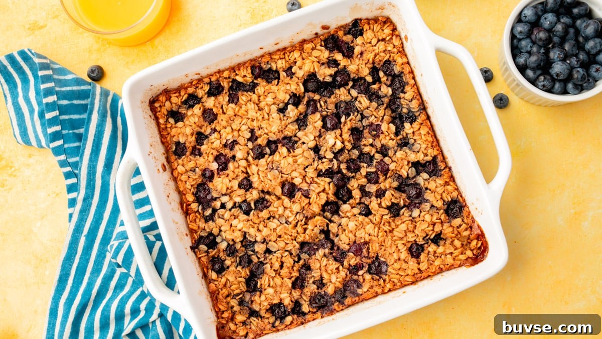 Blueberry Baked Oatmeal Recipe 15 An overhead view of a baking dish with blueberry baked oatmeal in it with two glasses of orange juice and a bowl of blueberries on the side.