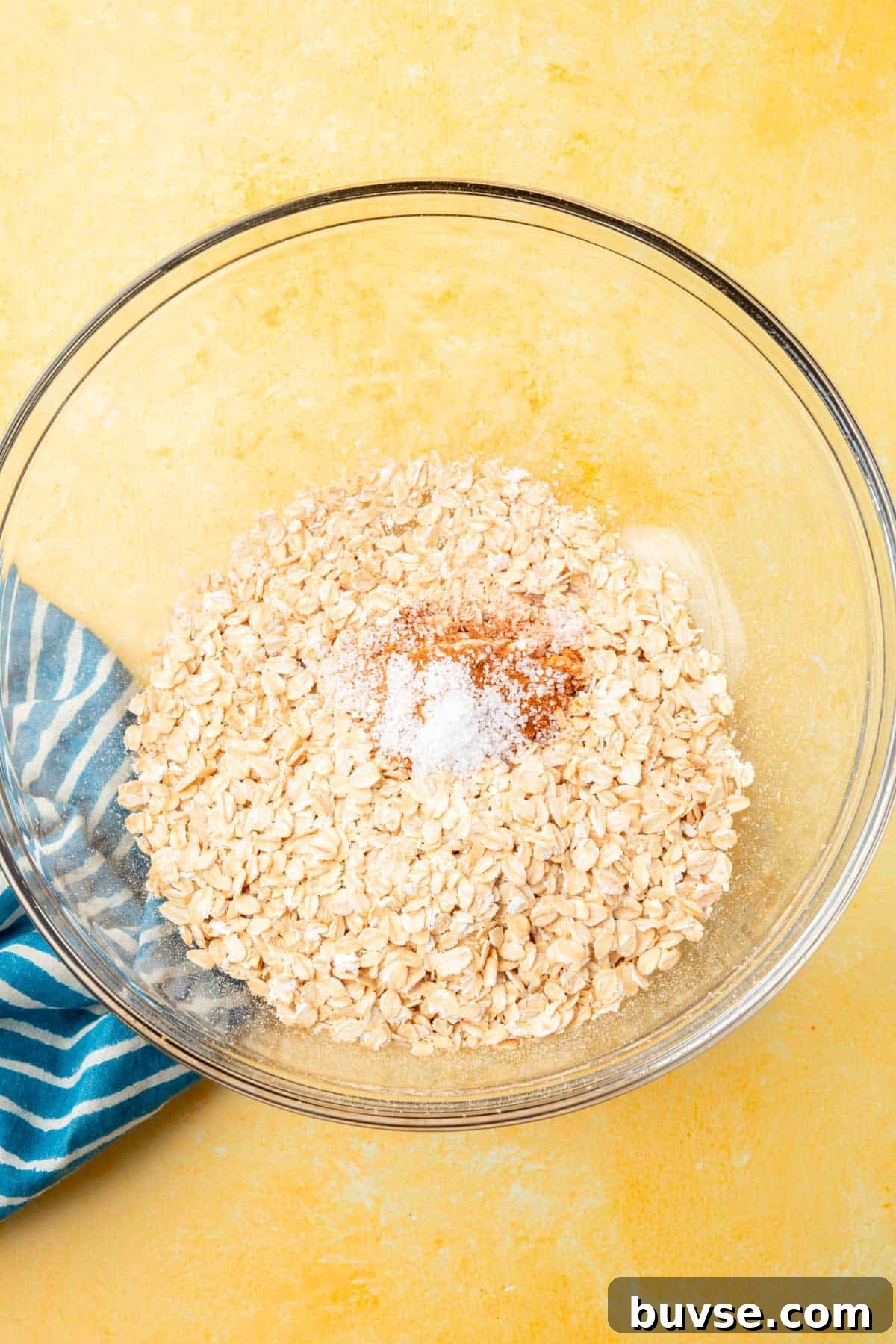 Blueberry Baked Oatmeal Recipe 4 A glass mixing bowl filled with gluten-free oats, salt, baking powder, and cinnamon that has not yet been mixed together.