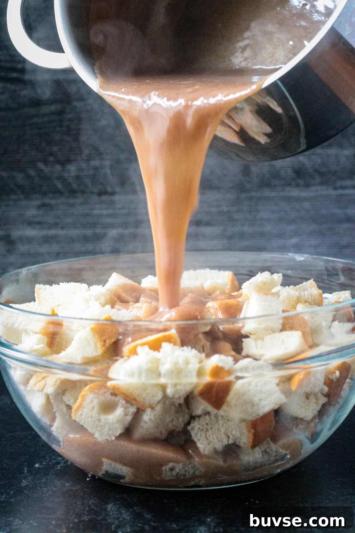 Creamy Vegan Bread Pudding Recipe with Cinnamon 10 Custard being poured from a sauce pot over the cubed bread.