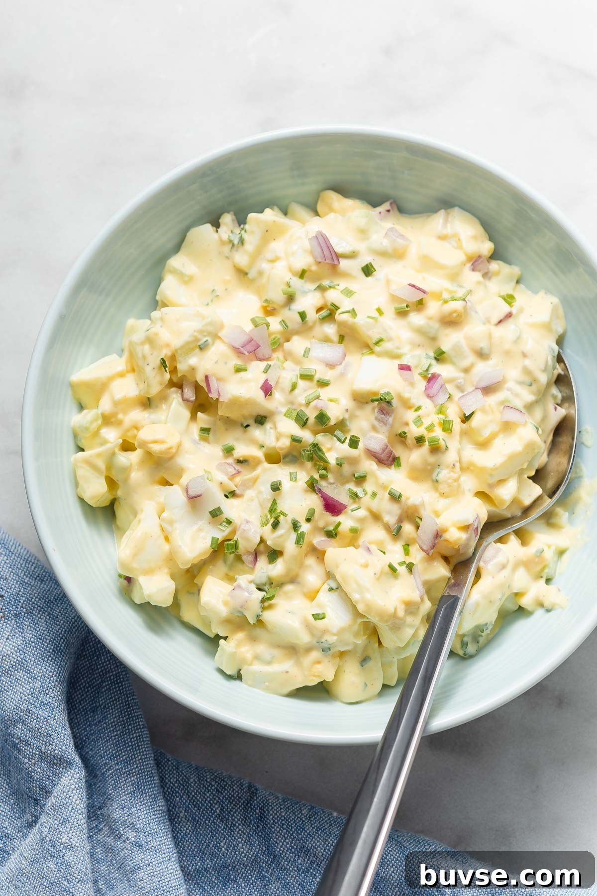 egg salad in a bowl with  spoon sprinkled with red onion and chives