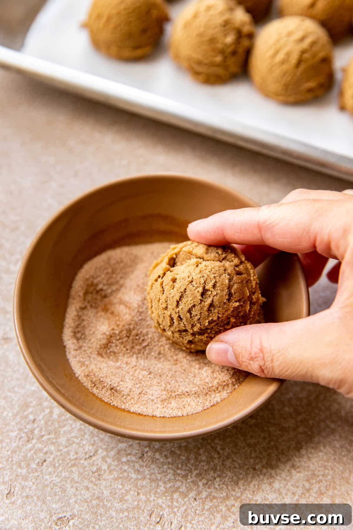 a womans hand rolling cookie dough in cinnamon and sugar.