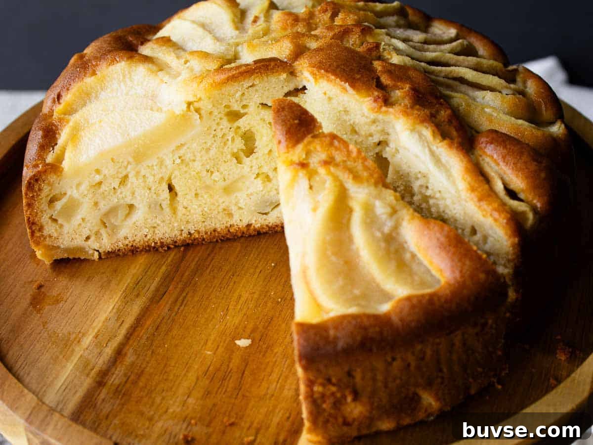 Cake with pear slices on top on a wooden cake stand with several wedges cut and removed.