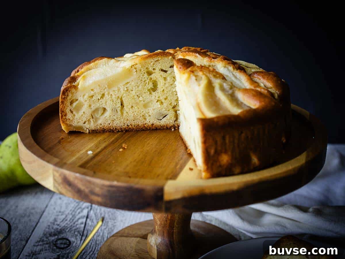 Cake topped with pear slices with a large wedge cut out on a cake stand made of wood.
