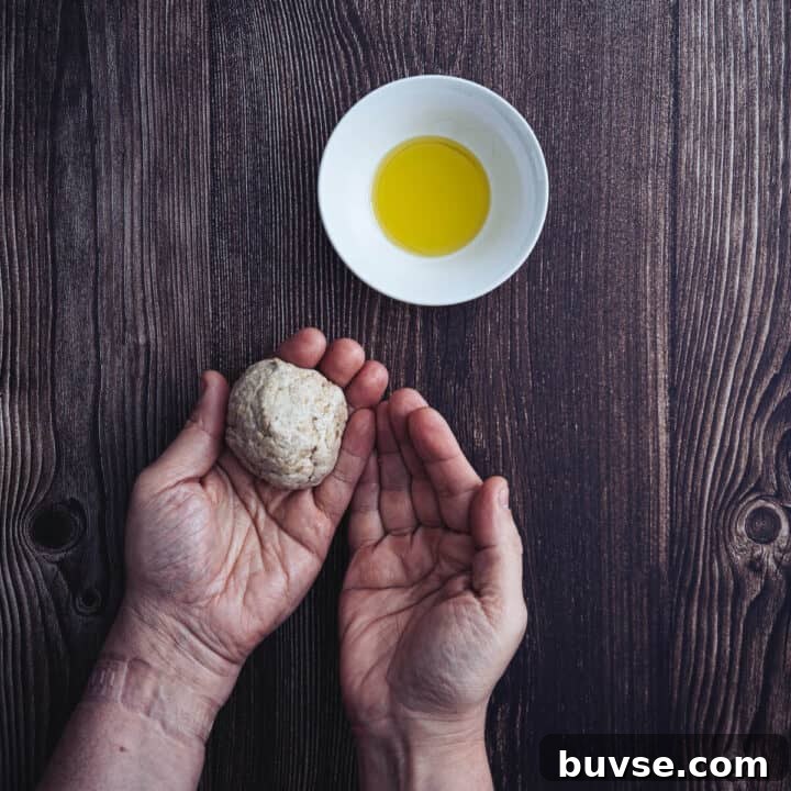 Gluten-Free Buckwheat Pita Bread Recipe 7 two hands holding buckwheat pita bread dough shaped into a ball with olive oil.