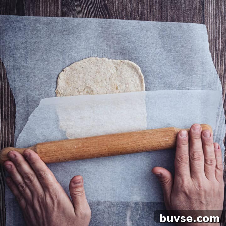 Gluten-Free Buckwheat Pita Bread Recipe 8 rolling out buckwheat pita bread between two sheets of parchment on a wooden surface.
